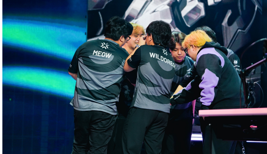 Valorant esports team huddling on stage before a match at an international tournament, wearing jerseys