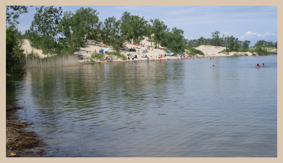 People relaxing on Outlet Beach, Sandbanks Provincial Park, with grassy sand dunes and Lake Ontario in the background — a popular nautical hideaway near Toronto.