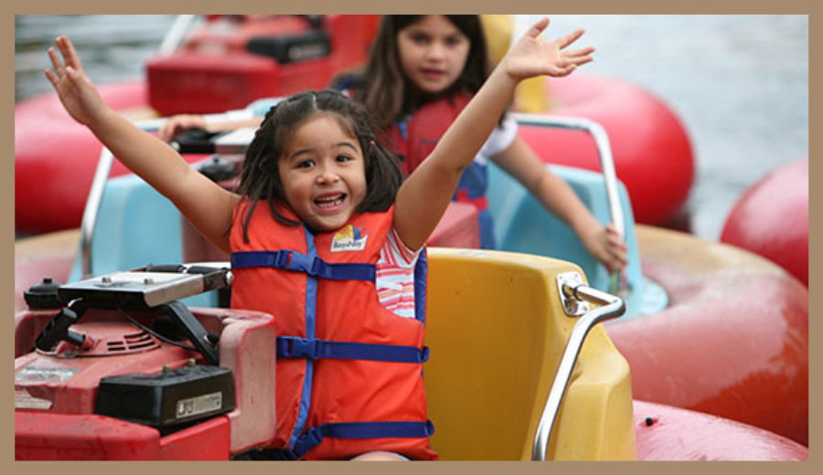 Children riding bumper boats at Centreville Amusement Park in Toronto, wearing life vests and smiling.