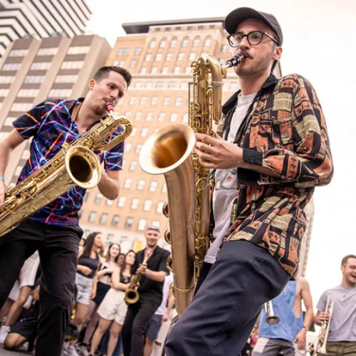 Saxophone duo ignites the streets with rhythm and flair at the 2025 Toronto Jazz Festival, drawing an enthusiastic crowd amid the city skyline.